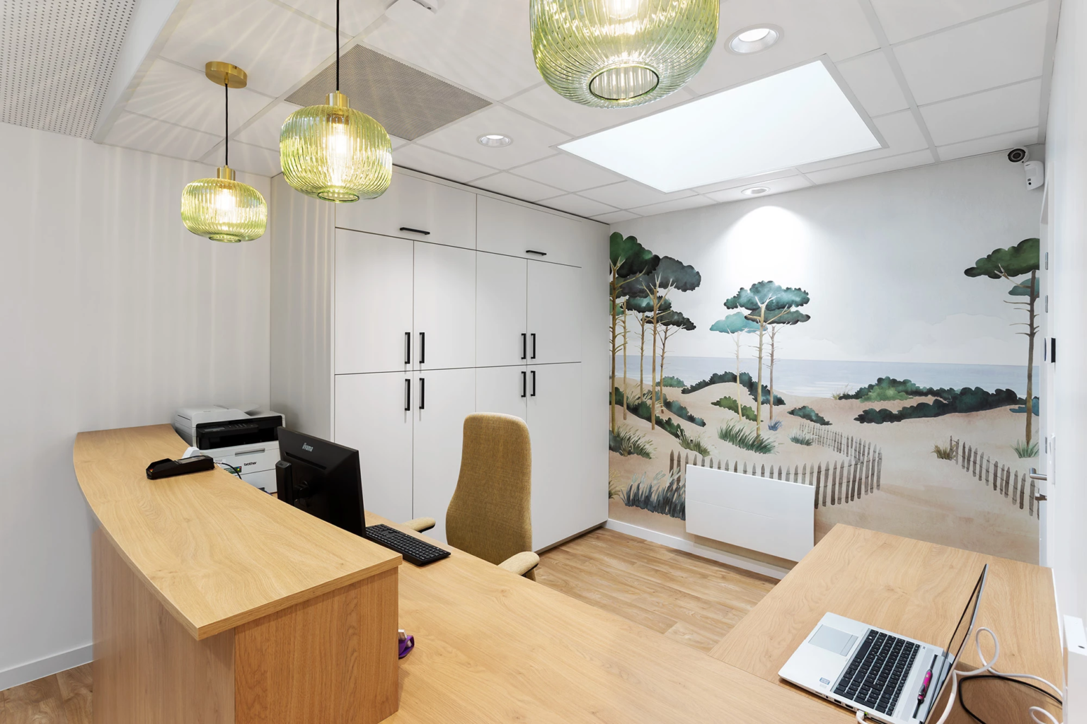 Bureau médical avec comptoir, ordinateur et fresque murale paysage