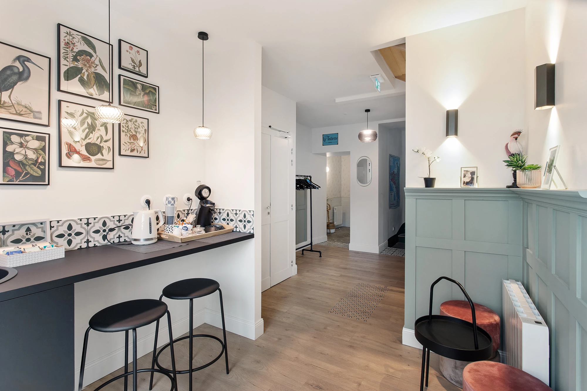 Espace accueil avec comptoir vert tabourets et cadres botaniques