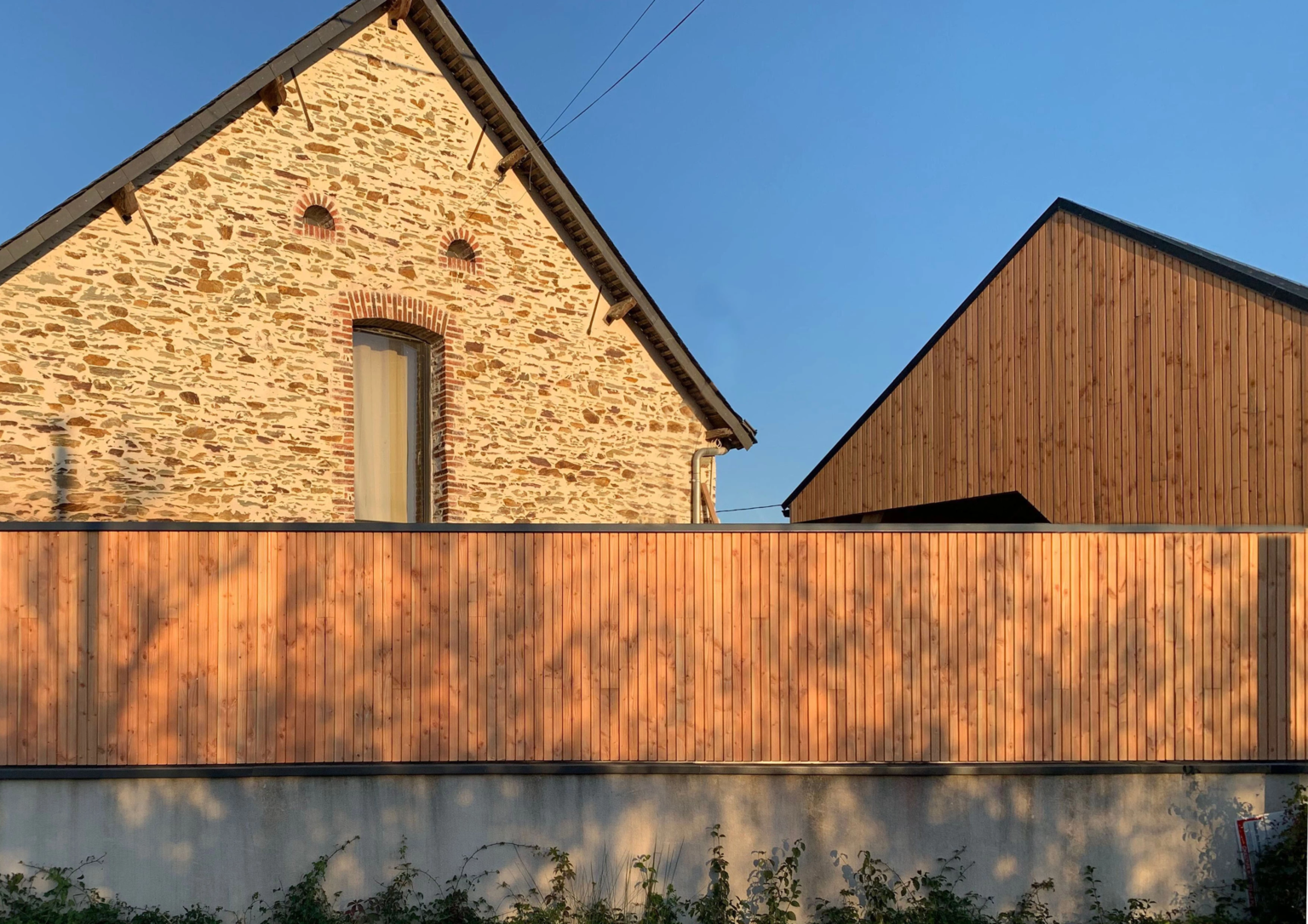 Maison en pierre et bâtiment en bois derrière palissade