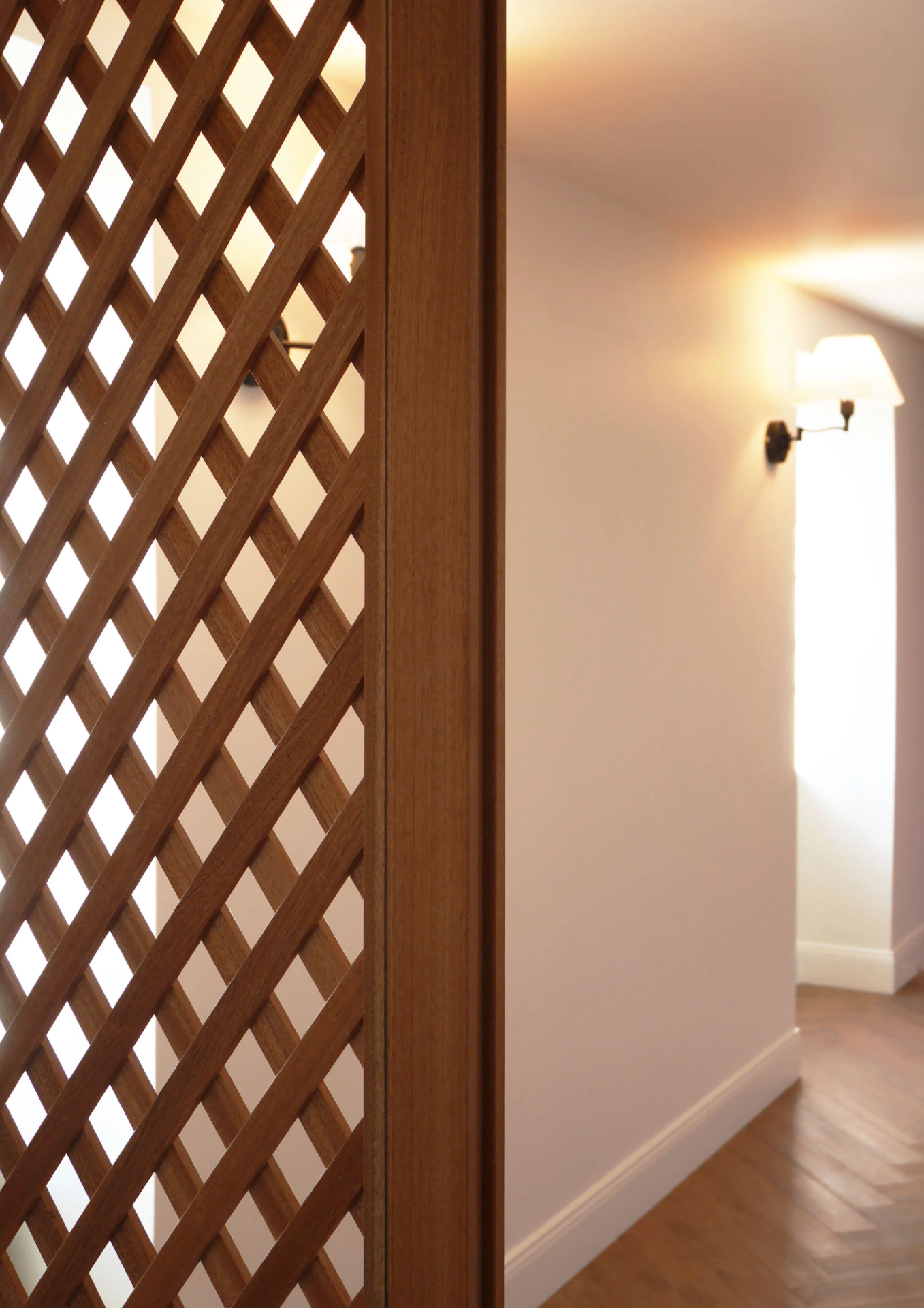 Détail de paroi en bois treillagé avec applique murale allumée dans un couloir lumineux.